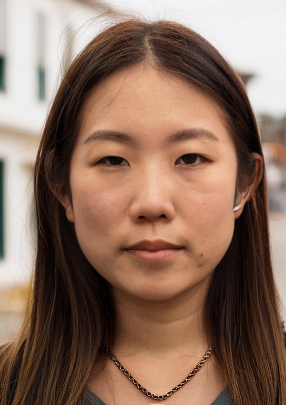 Asian woman in her 20s or 30s, smiling in front of a small town street